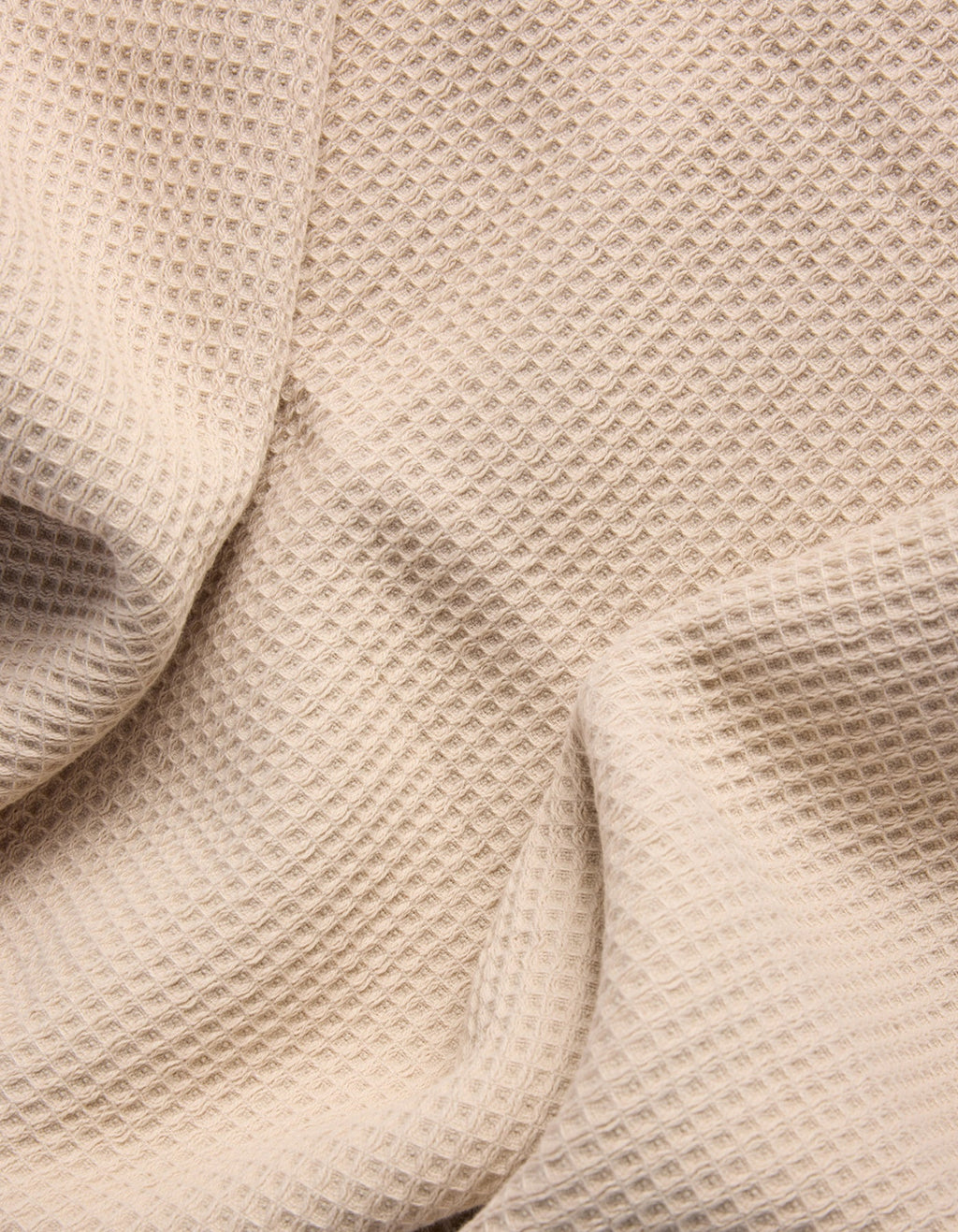 A close-up of Cozy Earth's Waffle Bath Sheets in beige, showing their textured, waffle-like pattern with gentle folds and shadows. |Color:Birch
