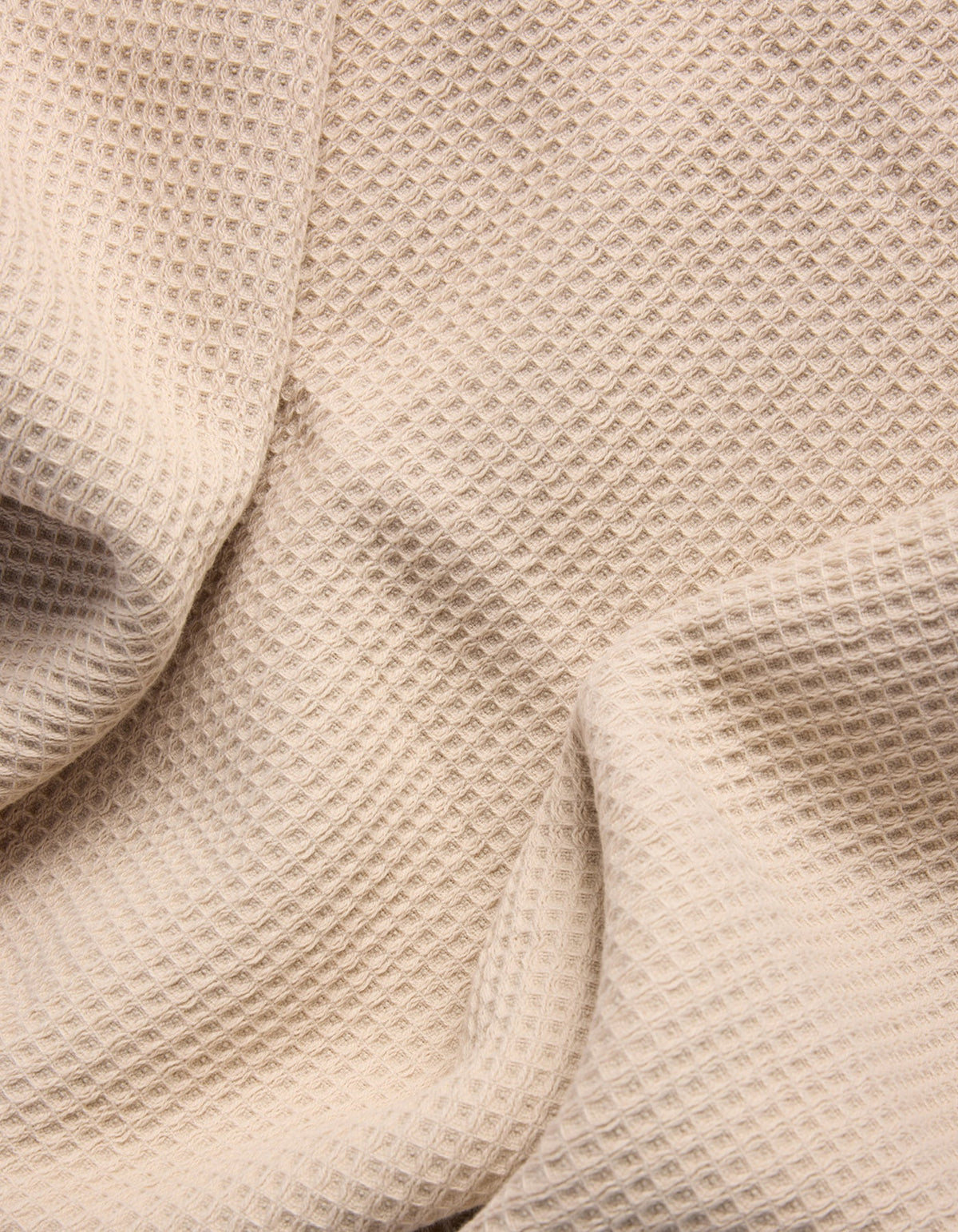 A close-up of Cozy Earth's Waffle Bath Sheets in beige, showing their textured, waffle-like pattern with gentle folds and shadows. |Color:Birch