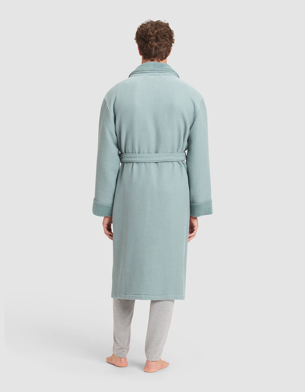 A person stands barefoot facing away, wearing the Cozy Earth Waffle Bath Robe with a belt over light gray pants, against a plain white background.  |Color:Brook