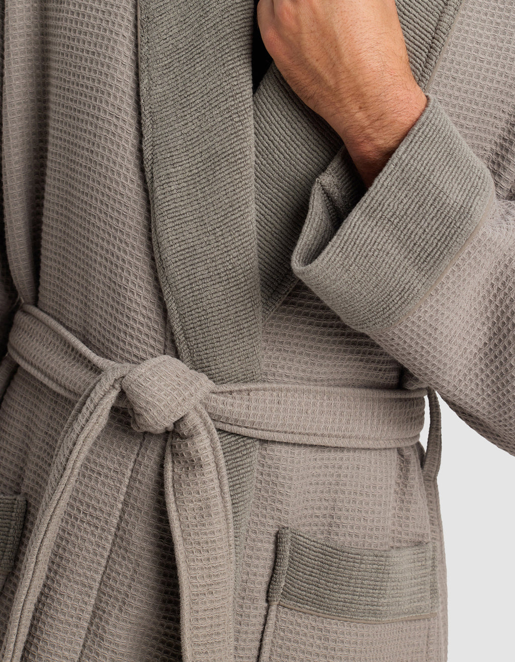 A person wears the Cozy Earth Waffle Bath Robe in light gray, featuring a textured design, shawl collar, waist tie, and two front pockets, with one hand holding the collar.|Color:Charcoal