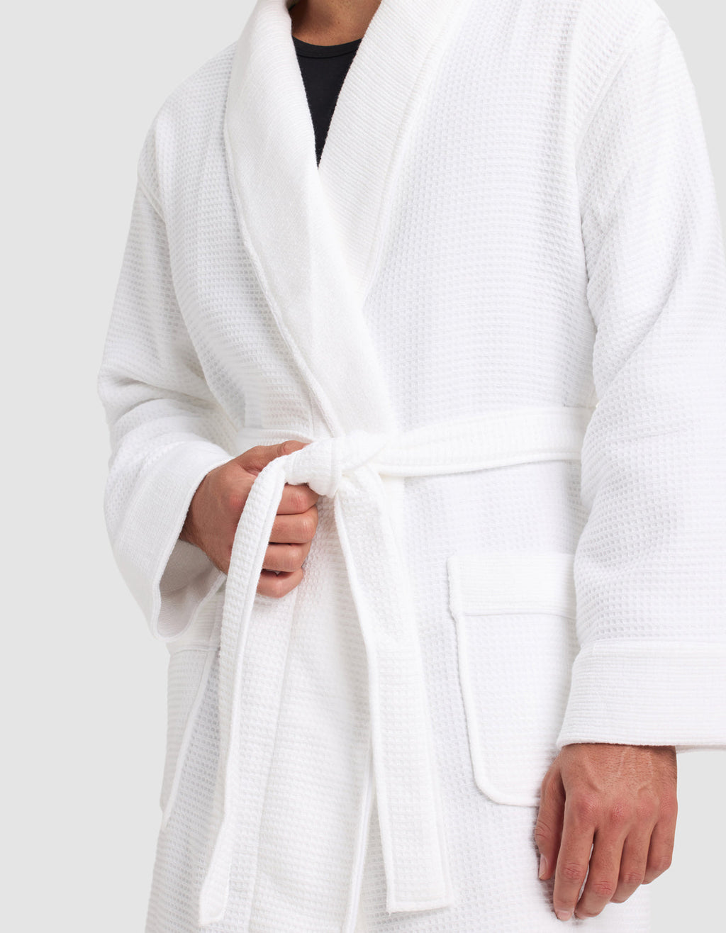 A person wears the Cozy Earth Waffle Bath Robe, tying its belt at the waist. Only their torso and hands are shown against a plain background.|Color:White