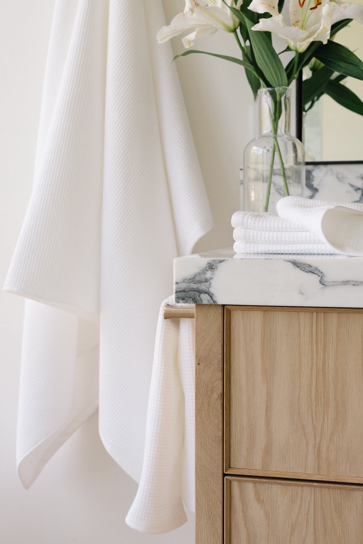 Waffle Bath Towel in the color White. Photo of White Waffle Bath Towel taken as the Waffle Bath Towel hangs from a bathroom wall from a towel. |Color:White