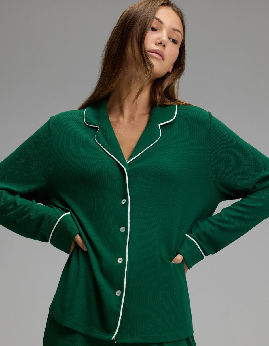 A woman stands with hands on hips, facing slightly to the side against a plain gray background, wearing the Cozy Earth Women’s Bamboo Rib-Knit Classic Long Sleeve Pajama Top in green with white piping.|Color:Evergreen