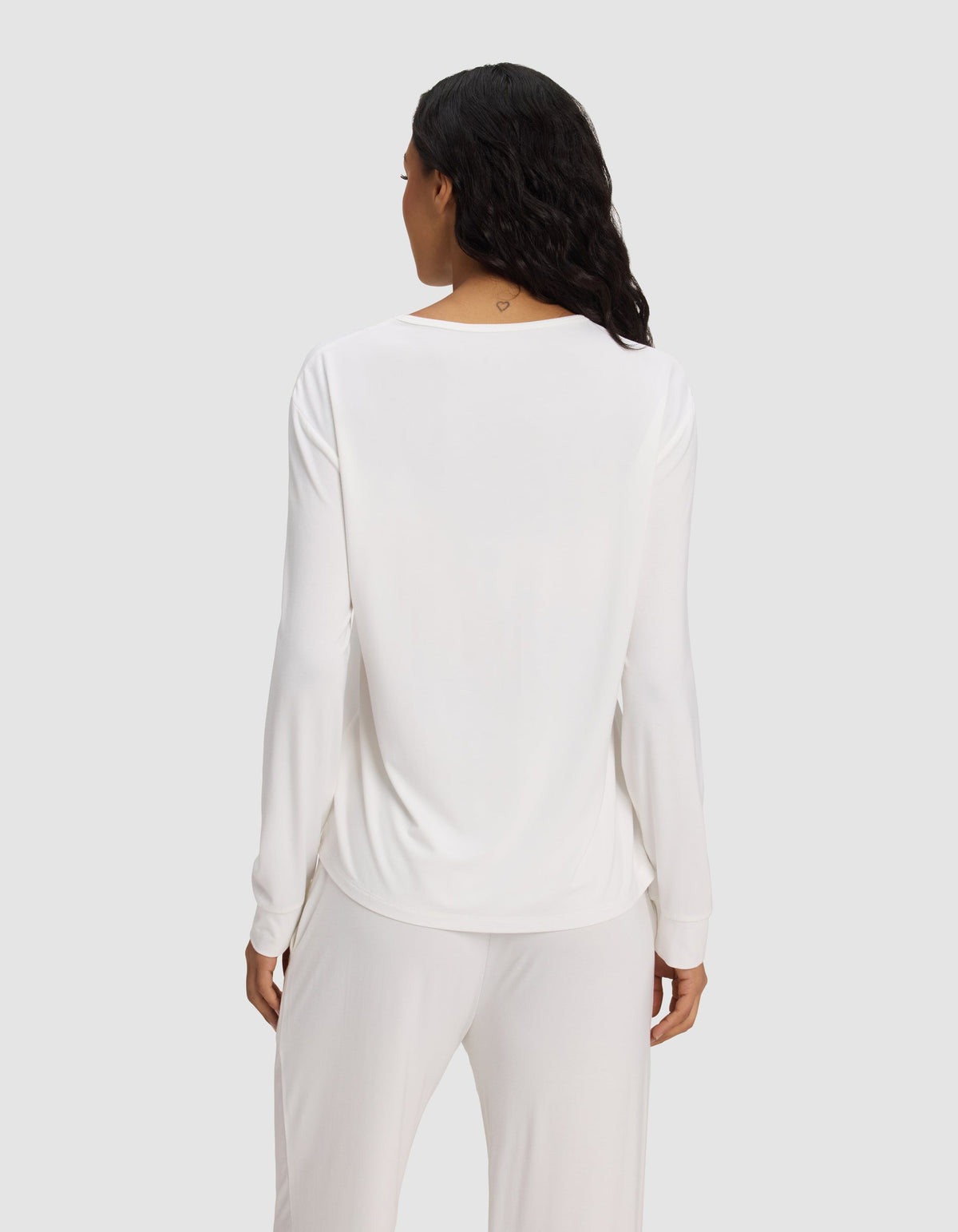 A woman with long dark hair is seen from the back, wearing the Cozy Earth Women's Bamboo Stretch-Knit Long Sleeve Lounge Tee in white, against a plain light gray background.|Color:Ivory
