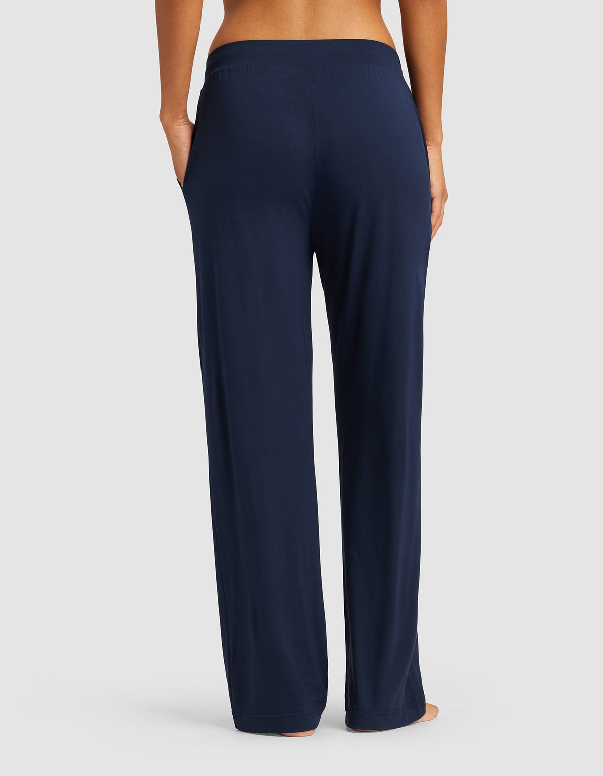 A woman is shown from the waist down, barefoot against a neutral background, wearing Cozy Earth Women's Bamboo Stretch-Knit Pant in navy blue with a relaxed fit and elastic waistband.|Color:Navy