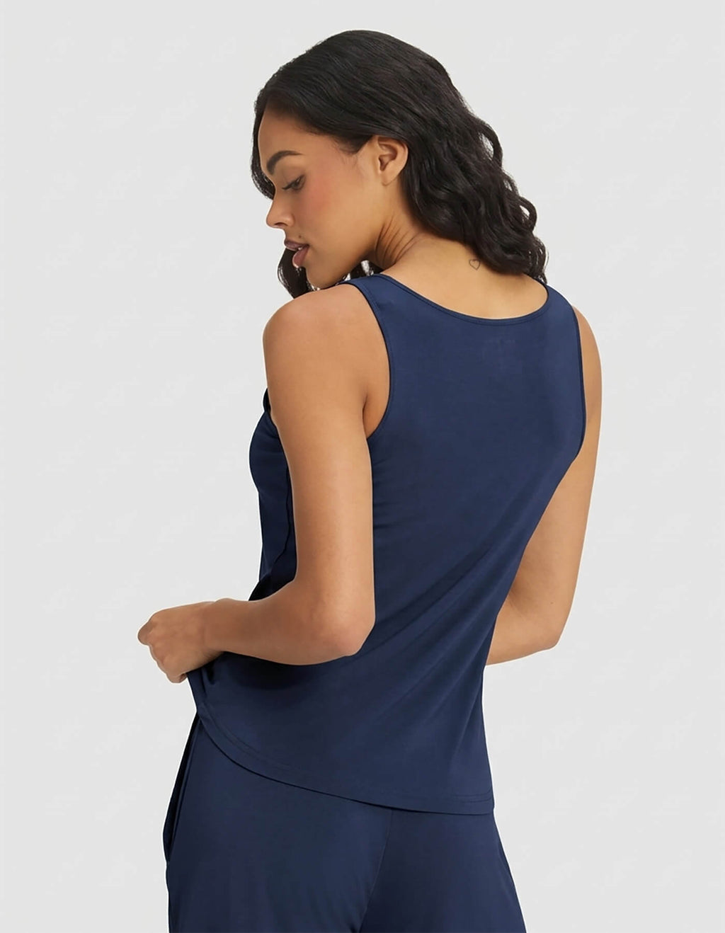 A woman with wavy dark hair is seen from the back wearing the Cozy Earth Women's Bamboo Stretch-Knit Tank & Short Set in navy blue, posed against a light gray background.|Color:Navy