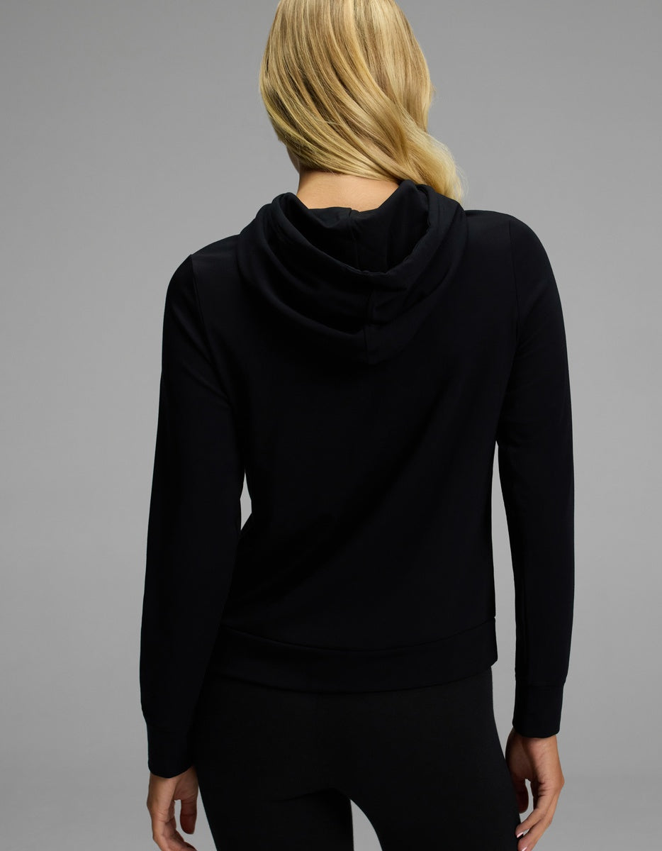 A woman with long blonde hair, seen from behind, is wearing the Cozy Earth Women’s Brushed Bamboo Hoodie and black pants against a plain gray background.|Color:Black