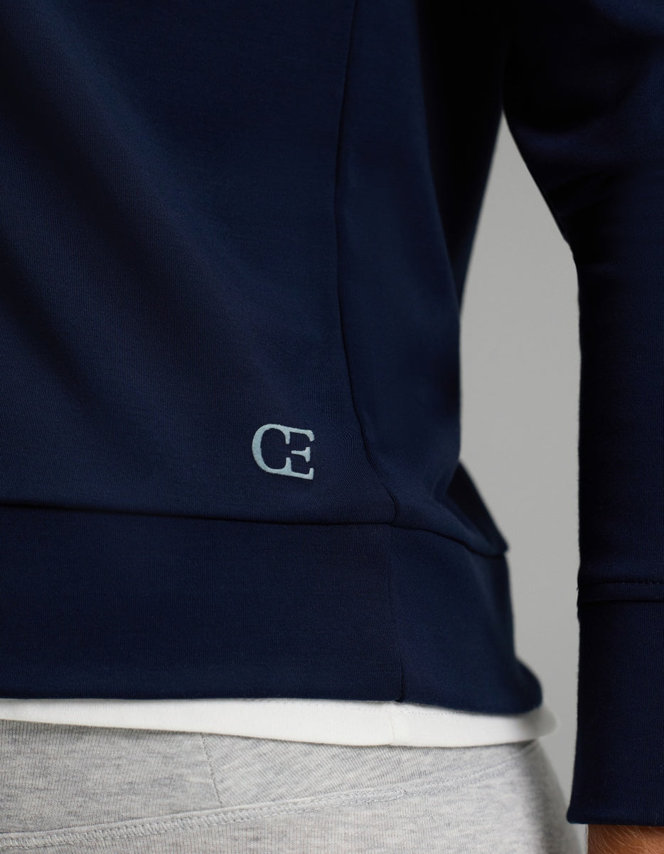 Close-up of a person wearing the Cozy Earth Women’s Brushed Bamboo Hoodie in navy blue with a small “CE” logo near the hem, layered over a white shirt and paired with light gray pants.|Color:Navy