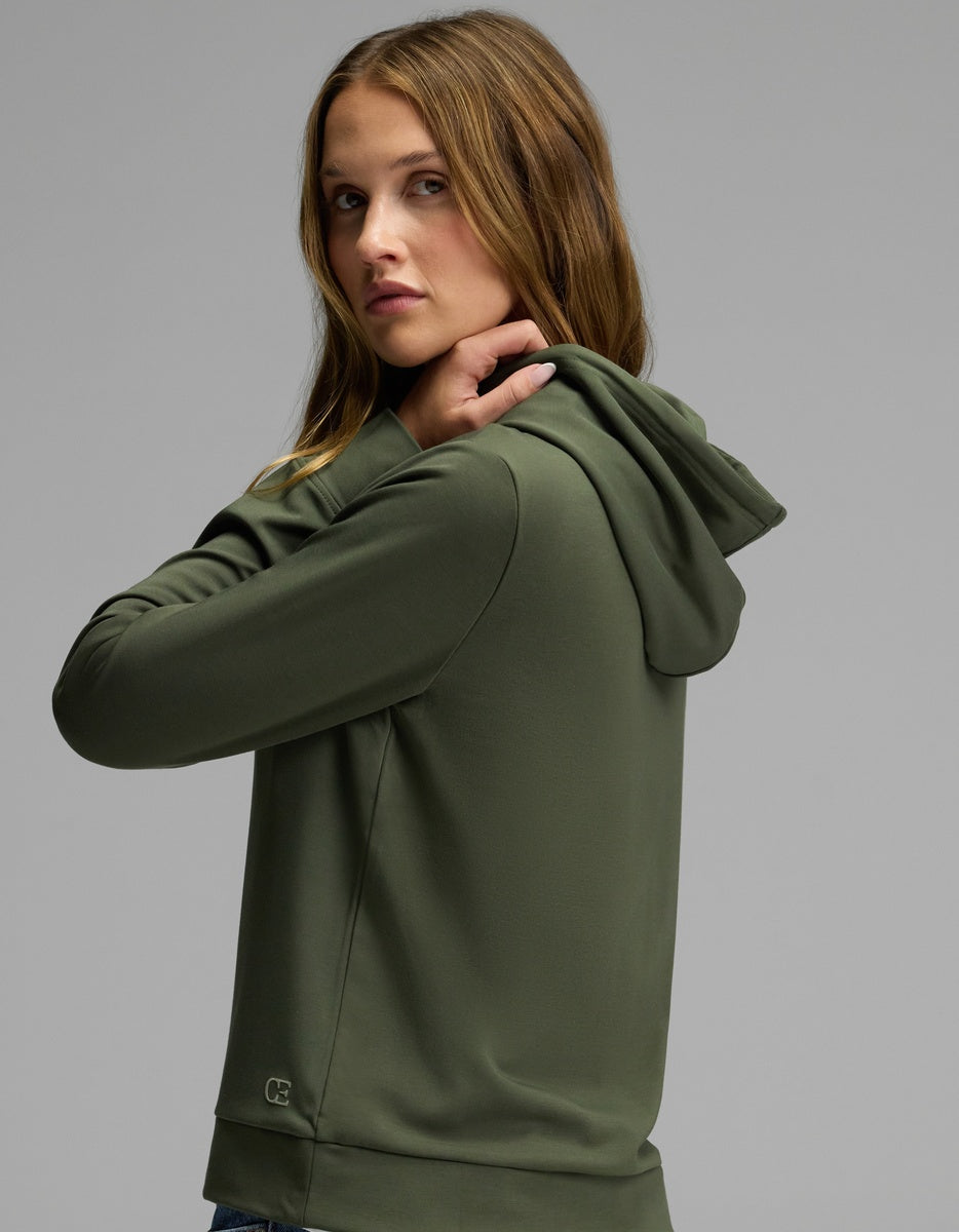 A woman models the Cozy Earth Women’s Brushed Bamboo Hoodie in olive green, glancing over her shoulder at the camera against a plain gray background.|Color:Olive