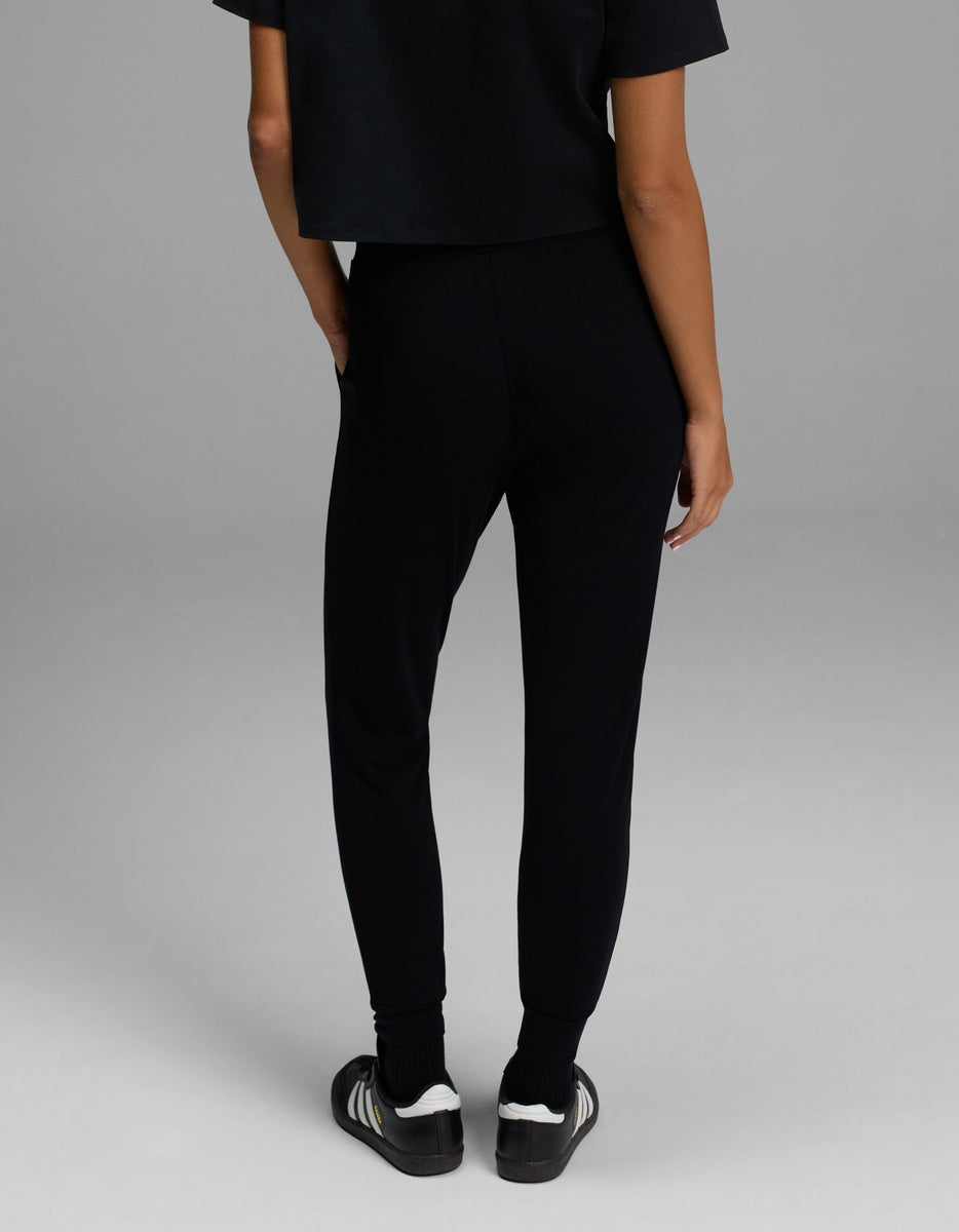 Shown from the back and standing against a gray background, a person is pictured wearing the Cozy Earth Women’s Brushed Bamboo Jogger in black. Only the lower half of the body is visible.|Color:Black