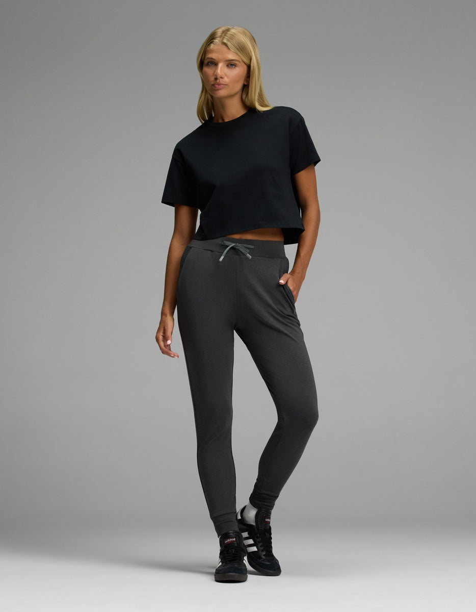 A woman poses in Cozy Earth’s Women’s Brushed Bamboo Jogger and a black crop t-shirt paired with black sneakers against a plain gray background.|Color:Charcoal