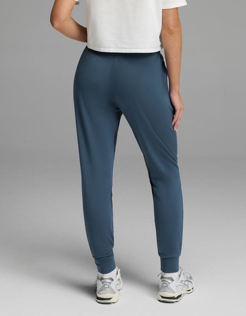 A person is seen from the back, wearing a white cropped T-shirt, white sneakers, and Cozy Earth’s Women’s Brushed Bamboo Jogger in blue, standing against a plain gray background.|Color:Dawn
