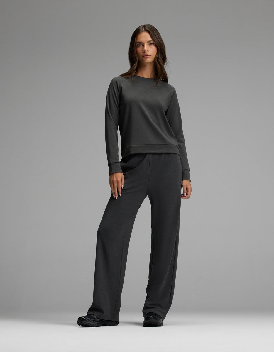 A woman stands against a gray background wearing the Cozy Earth Women’s Brushed Bamboo Pullover Crew in dark gray, paired with matching wide-leg pants, her posture relaxed and expression neutral.|Color:Charcoal