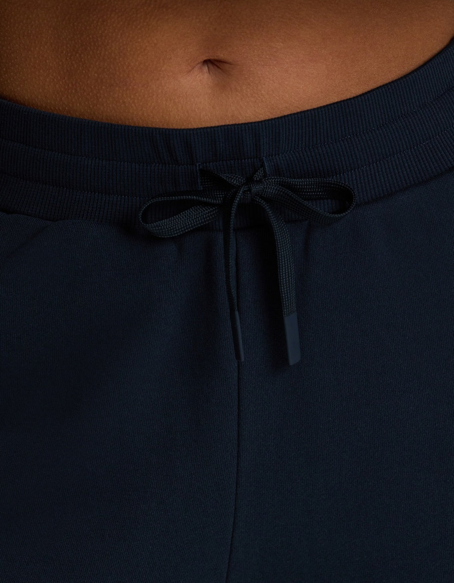 Close-up of a person’s lower torso wearing Cozy Earth Women’s Chelsea Pant in dark navy, featuring a visible tied bow at the waistband and part of the person’s belly button showing above the pants.|Color:Eclipse