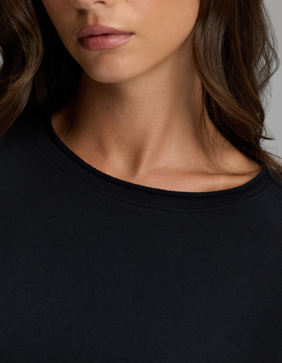 A close-up of a woman wearing the Cozy Earth Women’s Chelsea Pullover in black, showing her neck, part of her face, and wavy brown hair.|Color:Jet Black