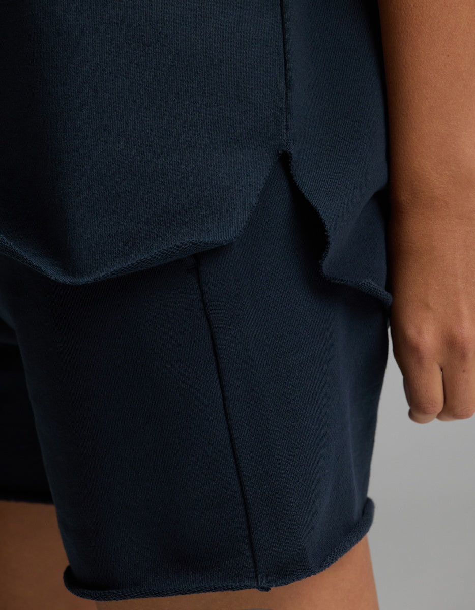 A close-up of a person’s hand resting by their side, wearing the Cozy Earth Women’s Chelsea Short Sleeve top in dark blue paired with matching shorts featuring raw, unfinished edges.|Color:Eclipse