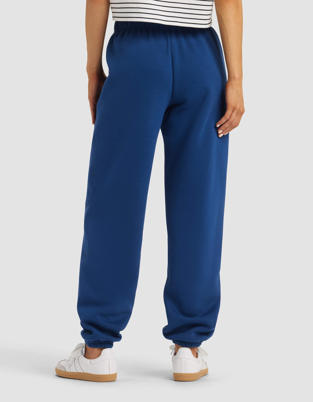 A person stands with their back to the camera, wearing a striped shirt, white sneakers, and Cozy Earth Women's Cityscape Sweatpant featuring an elastic waistband and cuffs.|Color:Pacific