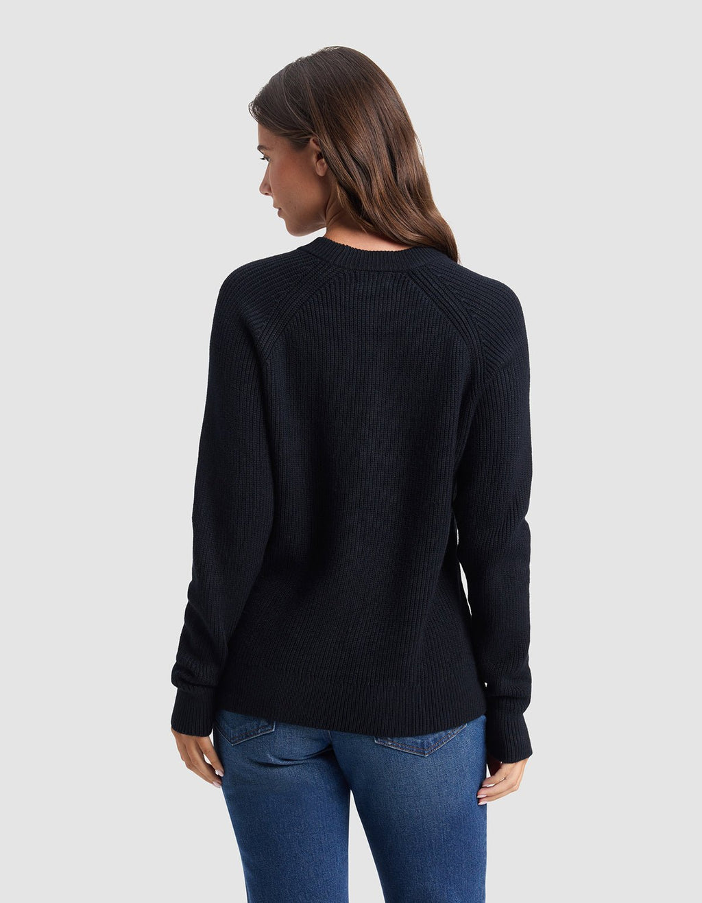 A woman with long brown hair, wearing the Cozy Earth Women's Classic Crewneck and blue jeans, stands facing away from the camera against a plain light gray background.|Color:Jet Black