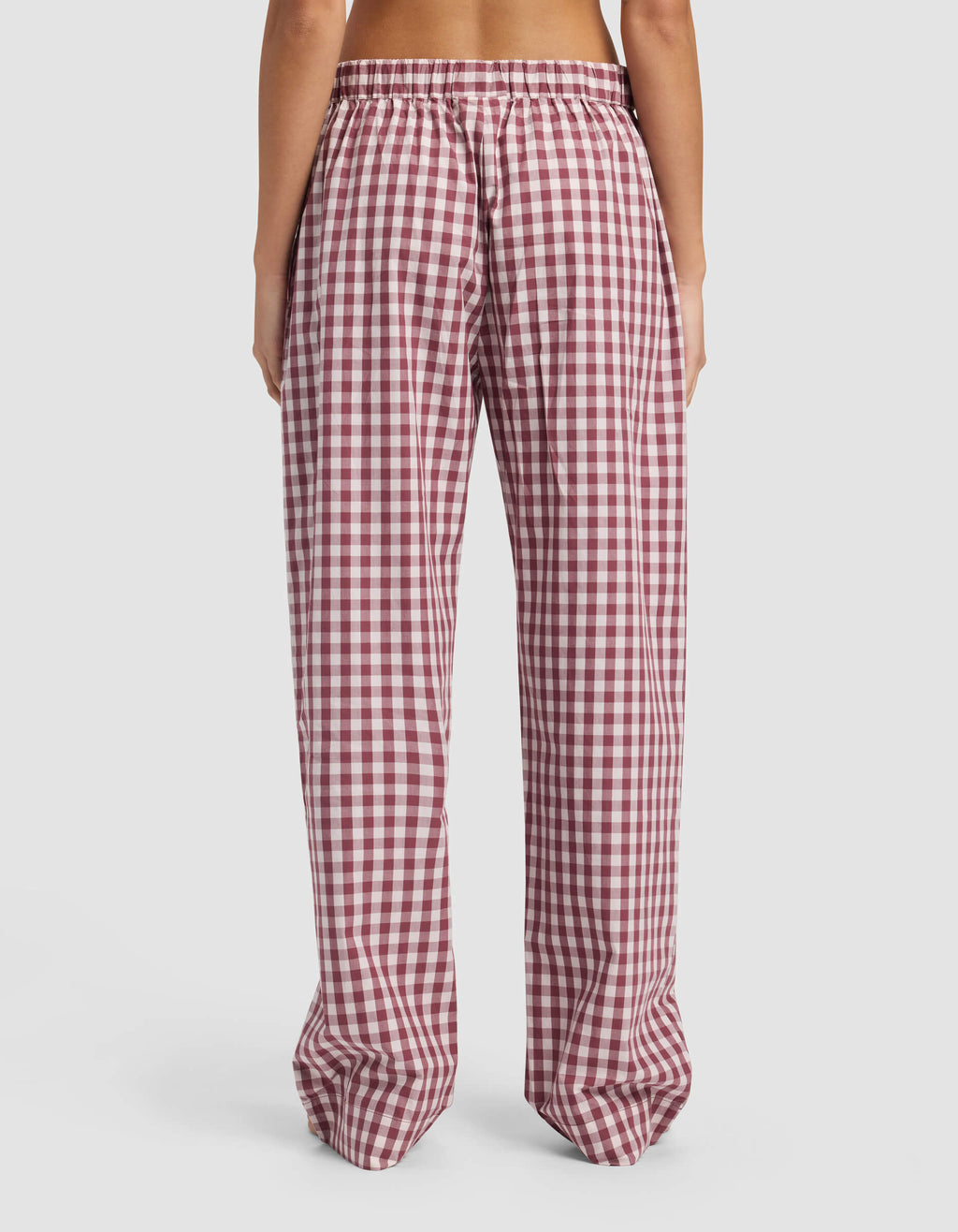 A person stands with their back to the camera, wearing Cozy Earth's Women's Sutton Pajama Pant—loose-fitting, high-waisted, red and white checkered with an elastic waistband—against a plain white background.|Color:Mulberry Gingham