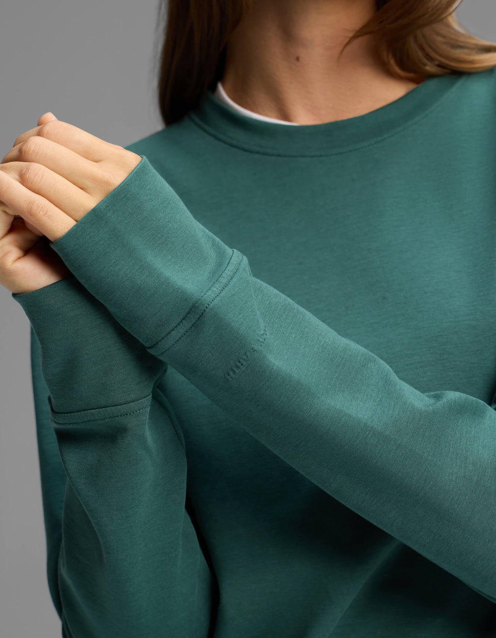 A person wearing the Cozy Earth Women's Versa Crewneck in teal clasps their hands together in front of their chest. The face is not visible, and the background is plain gray.|Color:Uniform