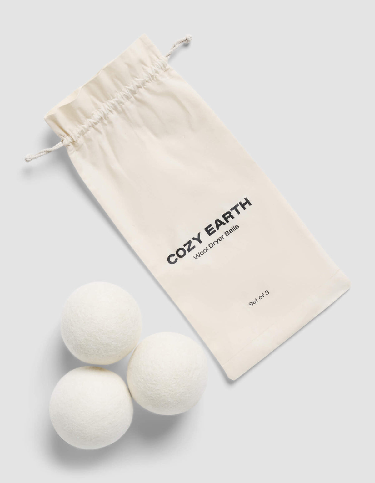 Three white Cozy Earth Dryer Balls with a Cozy Earth drawstring bag on a light gray background |Size:Regular