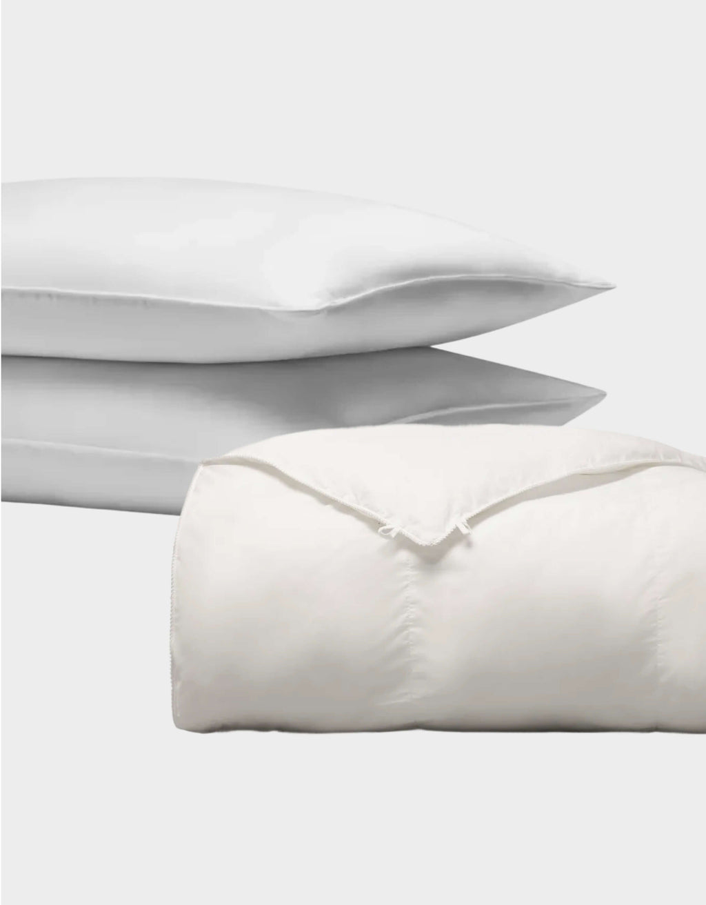 The Cozy Earth Down Alternative Insert Bundle features two white pillows stacked behind a neatly folded white comforter with visible seams and corner ties, all set against a plain, light background.|Filling:Lightweight