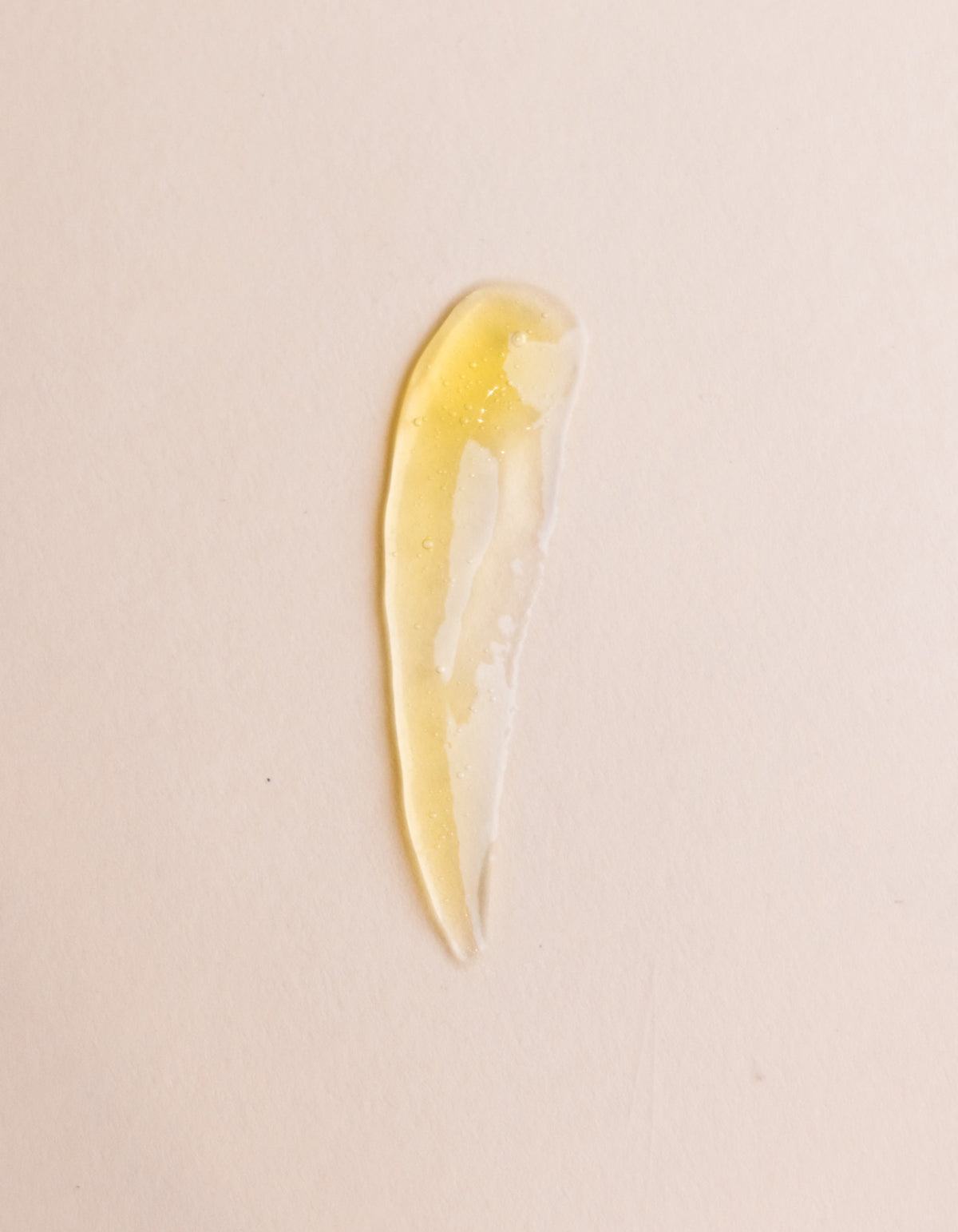 A translucent, yellow-tinted gel smear of Cozy Earth’s Enzyme Mask is spread in a curved, elongated shape on a light beige surface.|Size:Full Size
