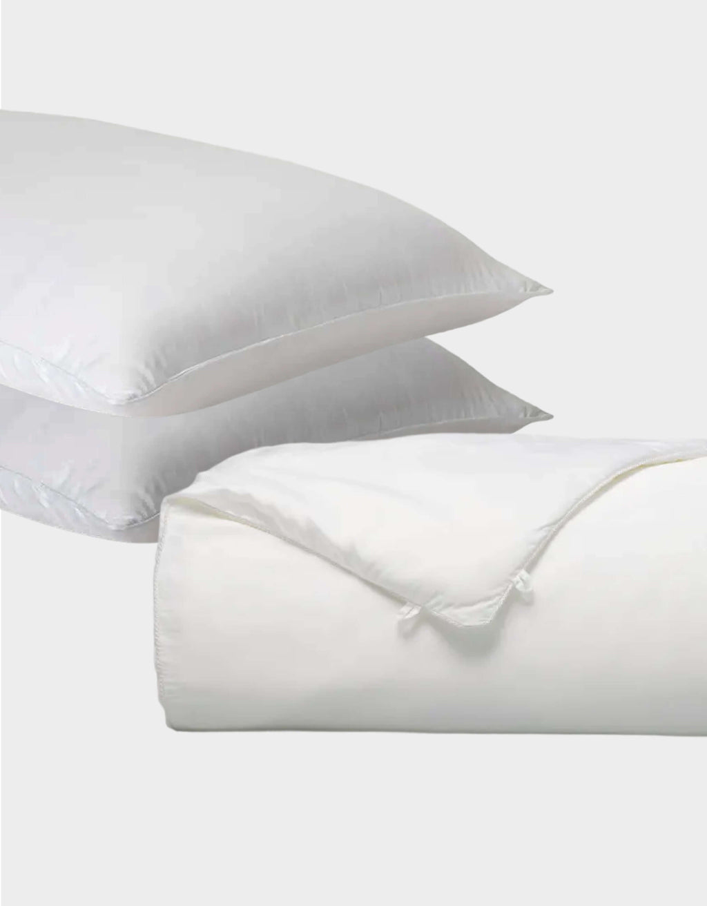 Two white Cozy Earth Silk Insert Bundle pillows are stacked, with a folded comforter featuring a tied corner in front, all set against a plain light gray background.|Filling:Extra