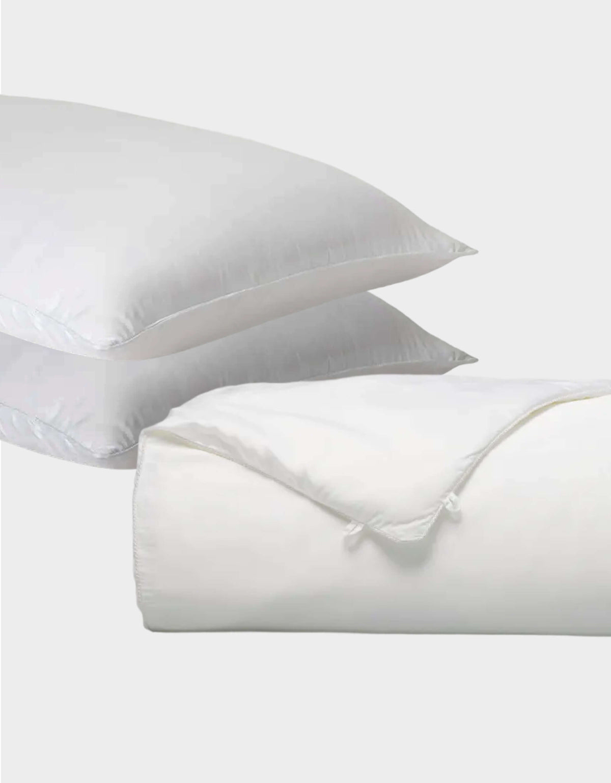 Two white Cozy Earth Silk Insert Bundle pillows are stacked, with a folded comforter featuring a tied corner in front, all set against a plain light gray background.|Filling:Extra